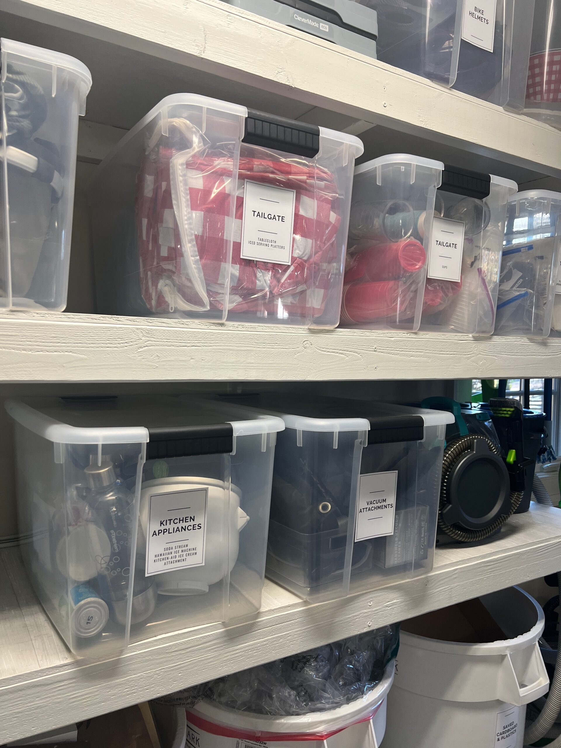 Garage shelving with clear plastic storage bins featuring large, easy-to-read labels, organizing items such as tools, appliances, and sports equipment.