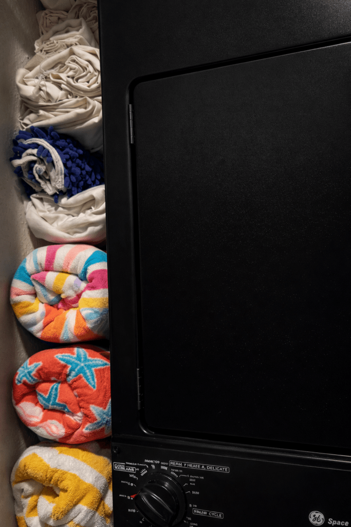 Wall-mounted towel rack in laundry closet storing rolled beach towels vertically for space-saving storage.